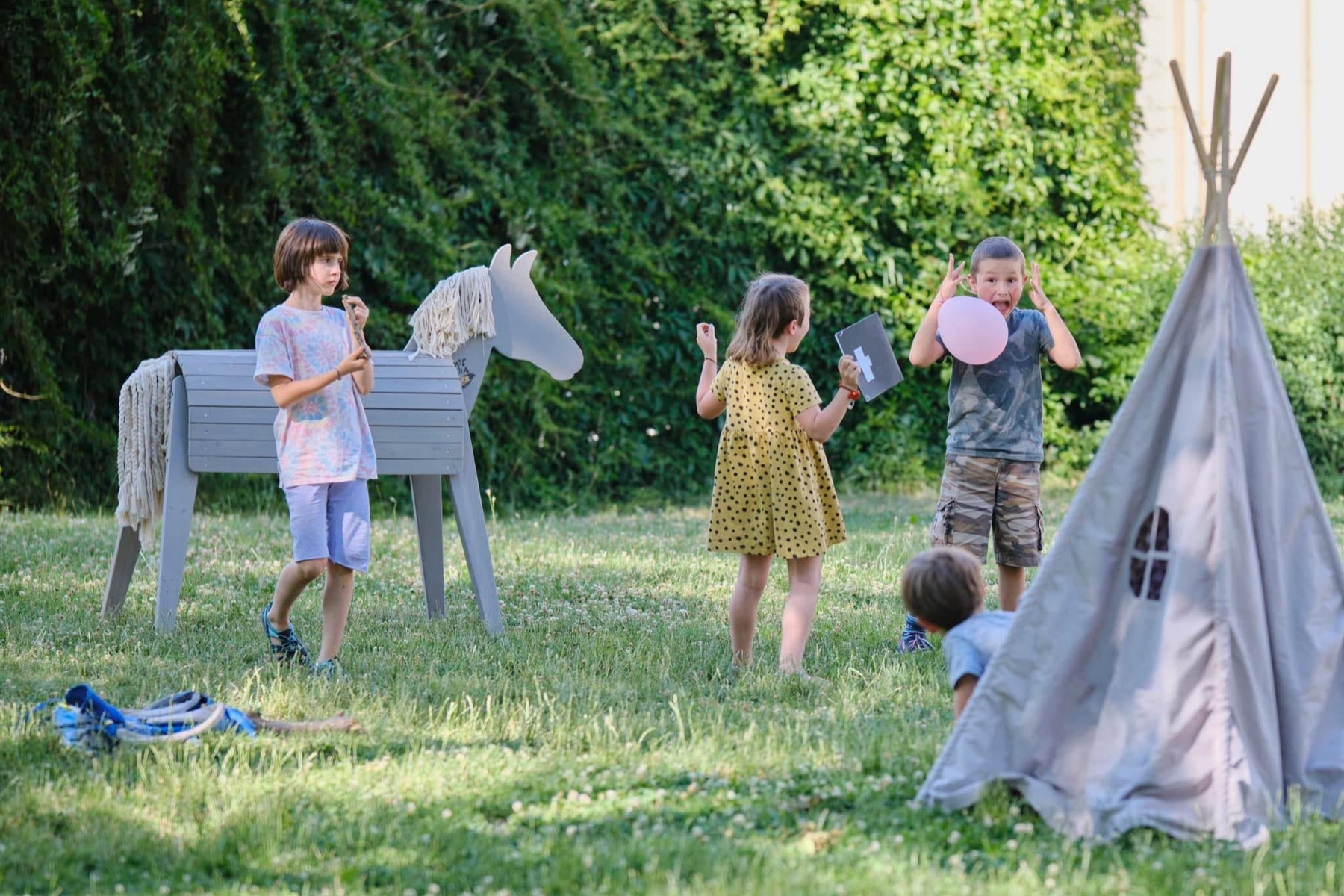 Děti společně připravují venkovní hru u dřevěného koně a teepee